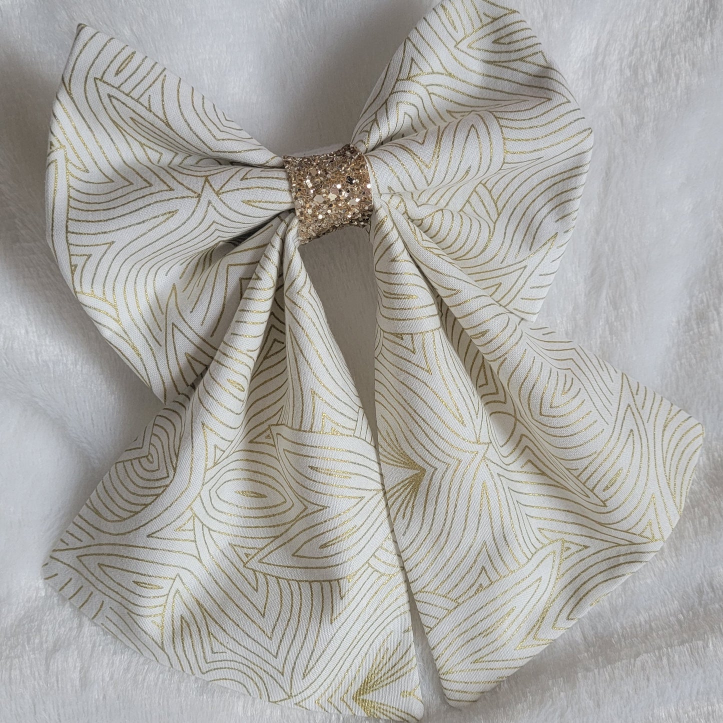 A handmade pet bow with a soft cotton print of abstract gold geometric lines on off-white background, gold blue glitter center sailor bow style with long showy tails.
