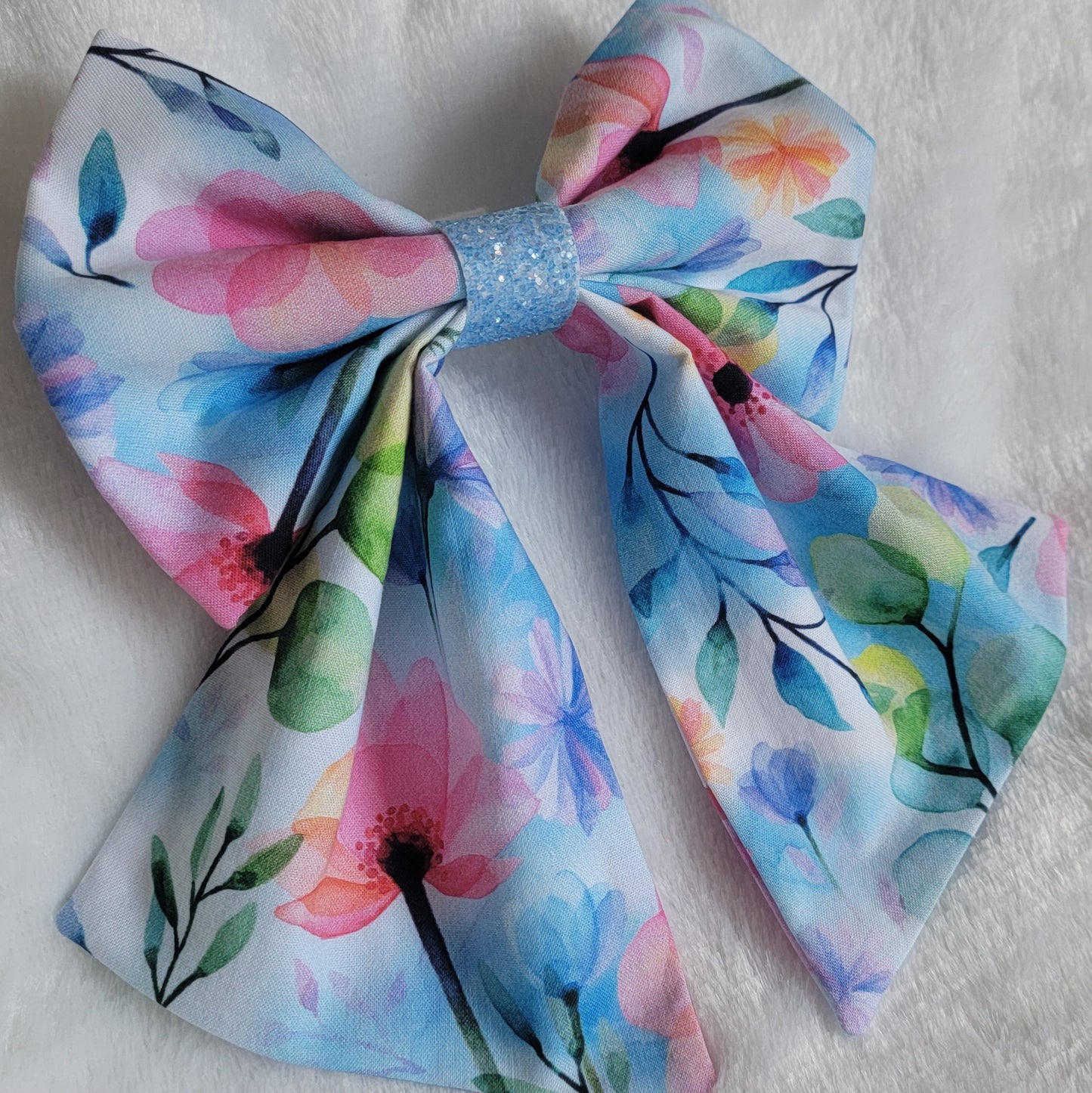 A handmade pet bow with a soft cotton print of watercolor florals in light blues pinks and greens, light blue glitter center sailor bow style with long showy tails.