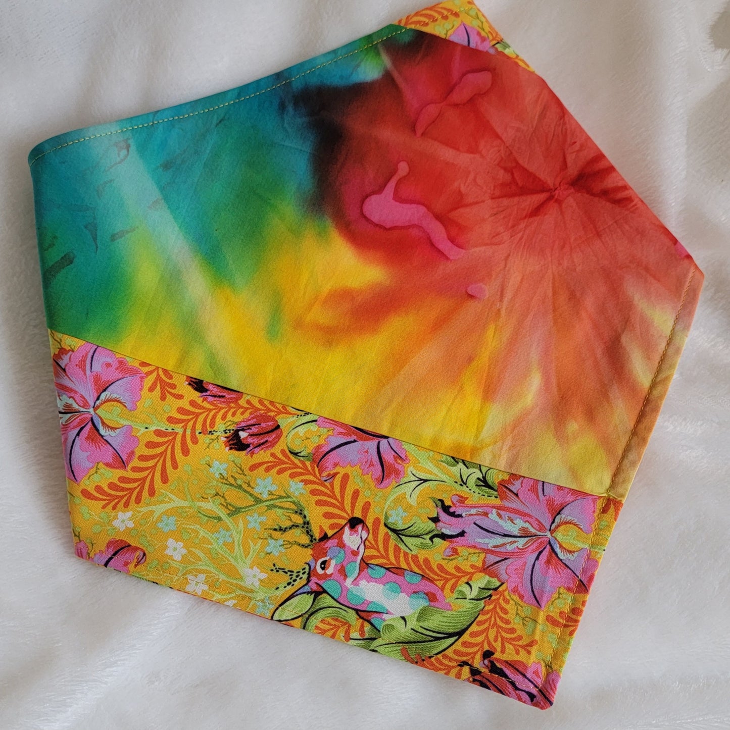 A multicolored pet bandana with stripes of cotton fabric featuring colorful rainbow tie-dye and vibrant floral stag print. Corners folded under showing side that has narrow edge stripe of stag floral fabric.