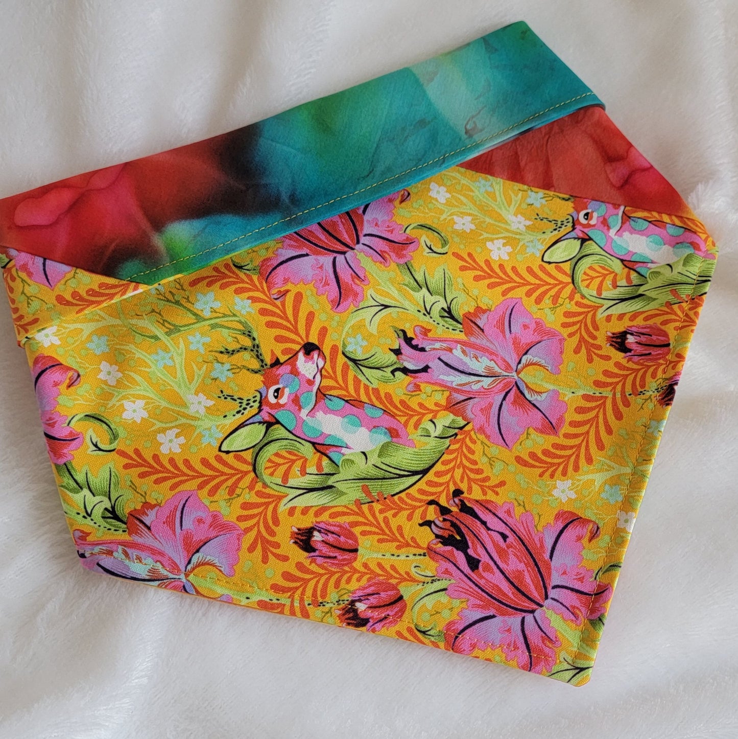 A multicolored pet bandana with stripes of cotton fabric featuring colorful rainbow tie-dye and vibrant floral stag print. Showing side that has wider stripe of stag floral fabric with folded corners and top to show edge or reverse side.