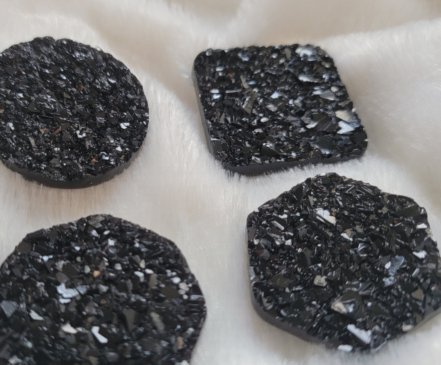 Four black crystal textured epoxy resin pieces - circle, octagon, square, and hexagon shaped - displayed on a white background