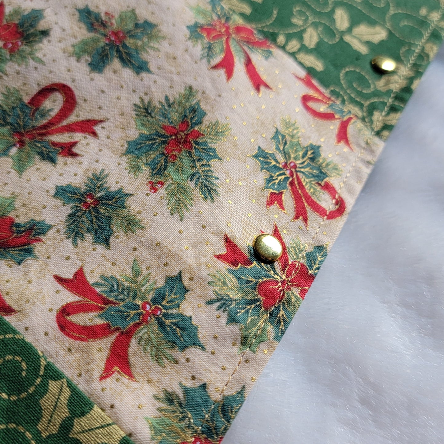 Close up of handmade fabric pet bandana featuring stripes of Christmas holiday themed fabric in mistletoe prints, with gold colored metal rivets along one edge.