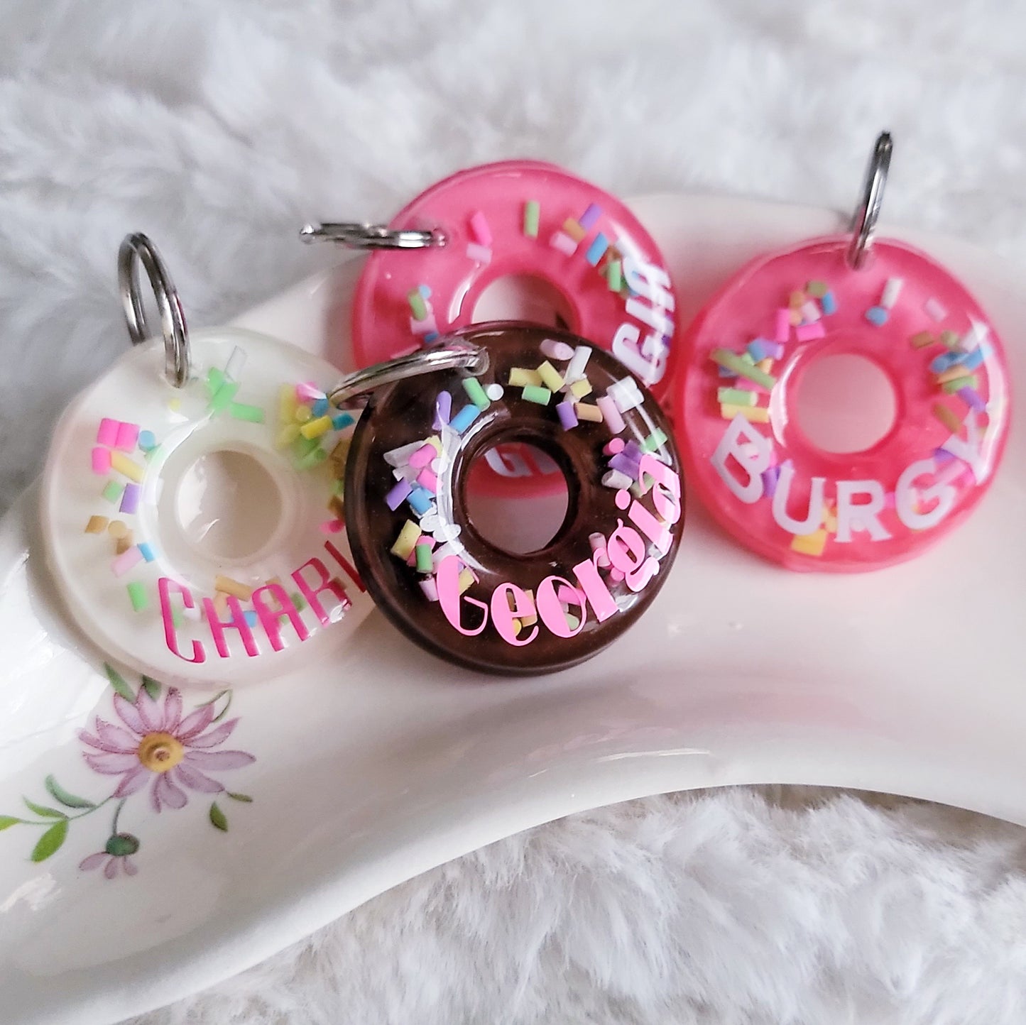Four epoxy resin pet tags with different names on them, pieces are made to look like rainbow sprinkle donuts with vanilla, chocolate and strawberry flavored icing.