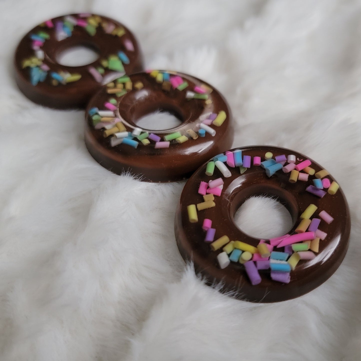 Three epoxy resin pieces made to look like chocolate donuts with rainbow sprinkles.