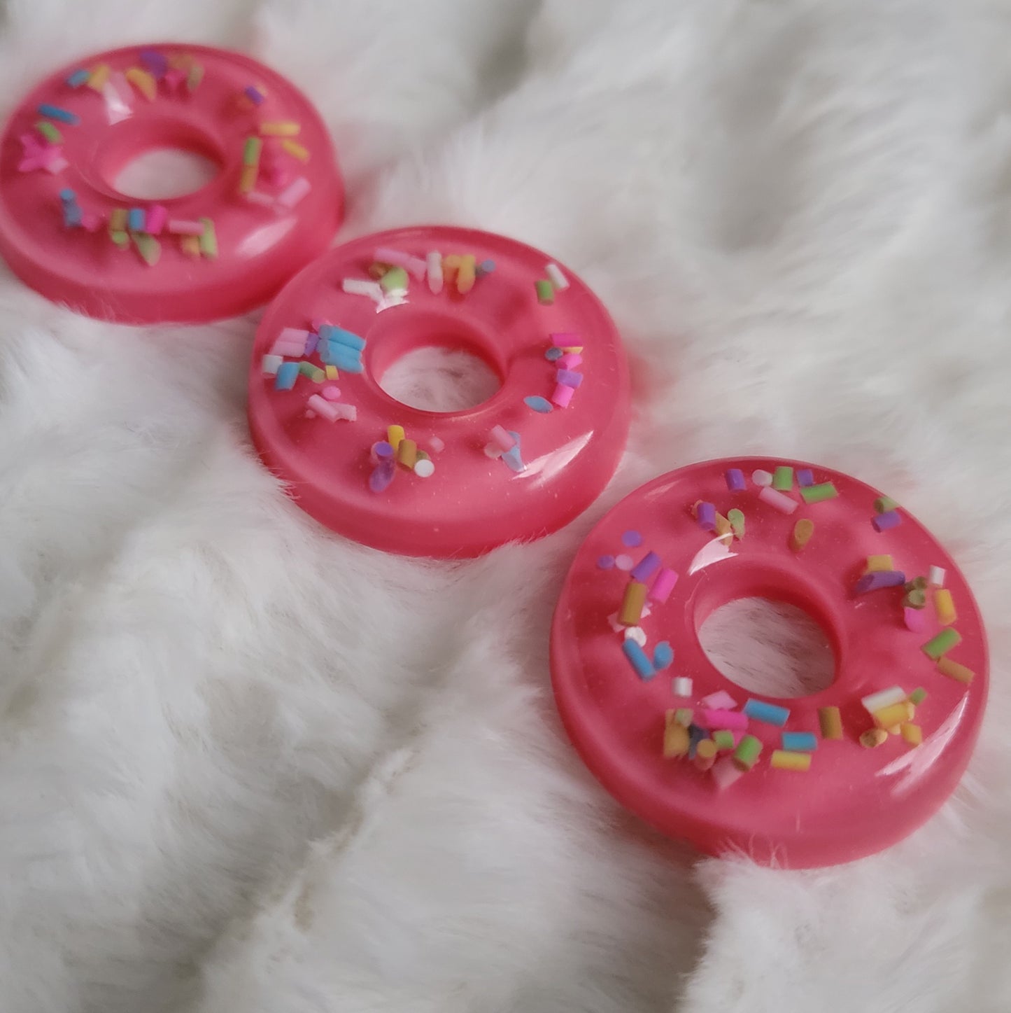 Three epoxy resin pieces made to look like strawberry donuts with rainbow sprinkles.