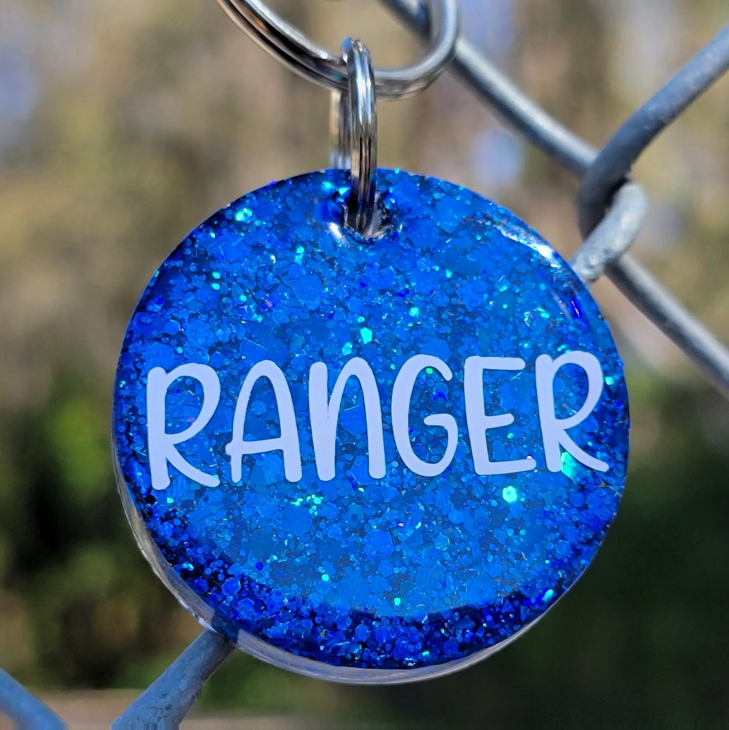 Round epoxy resin pet tag made with deep blue glitter and the name "Ranger" on it.