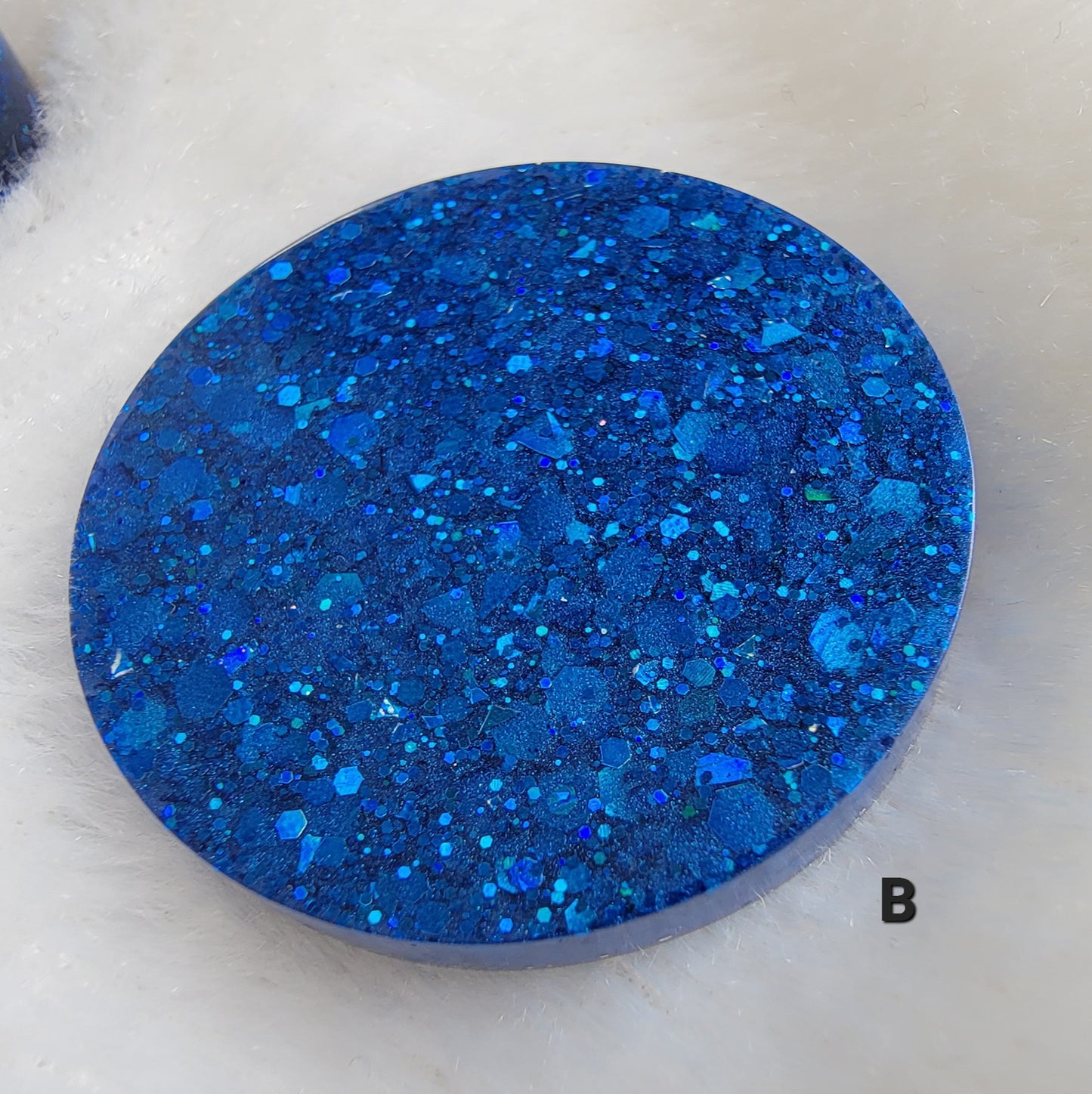 Close up of round epoxy resin piece made with deep blue glitter mixed with blue mica pigment.