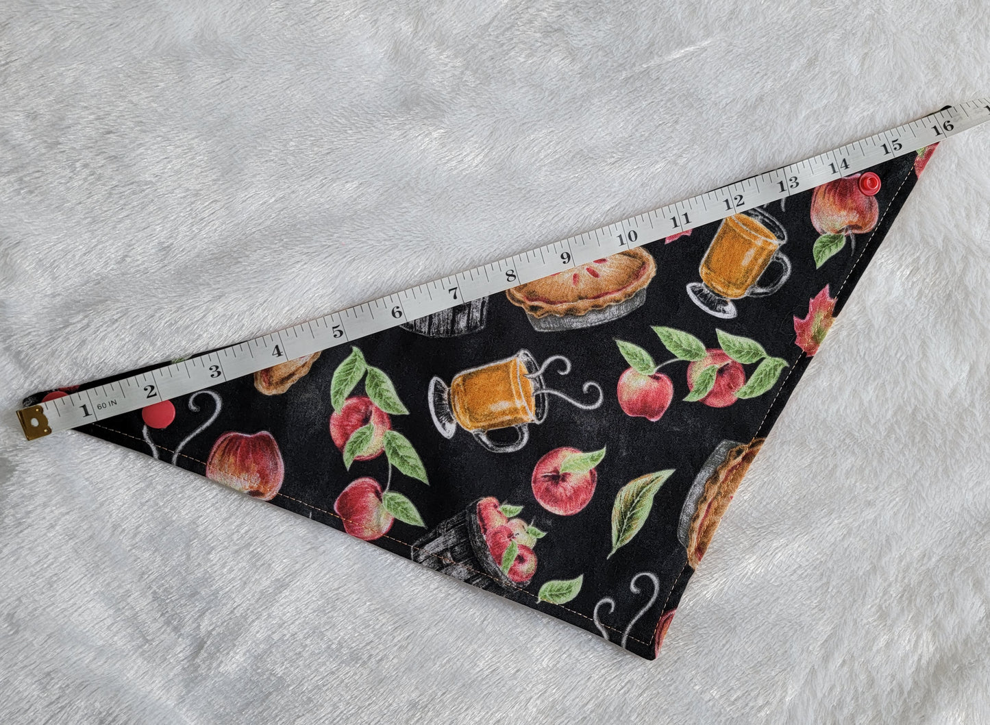 Bandana shown with measuring tape to show small size is 16", print is black with apples and apple treats like pies and cider.
