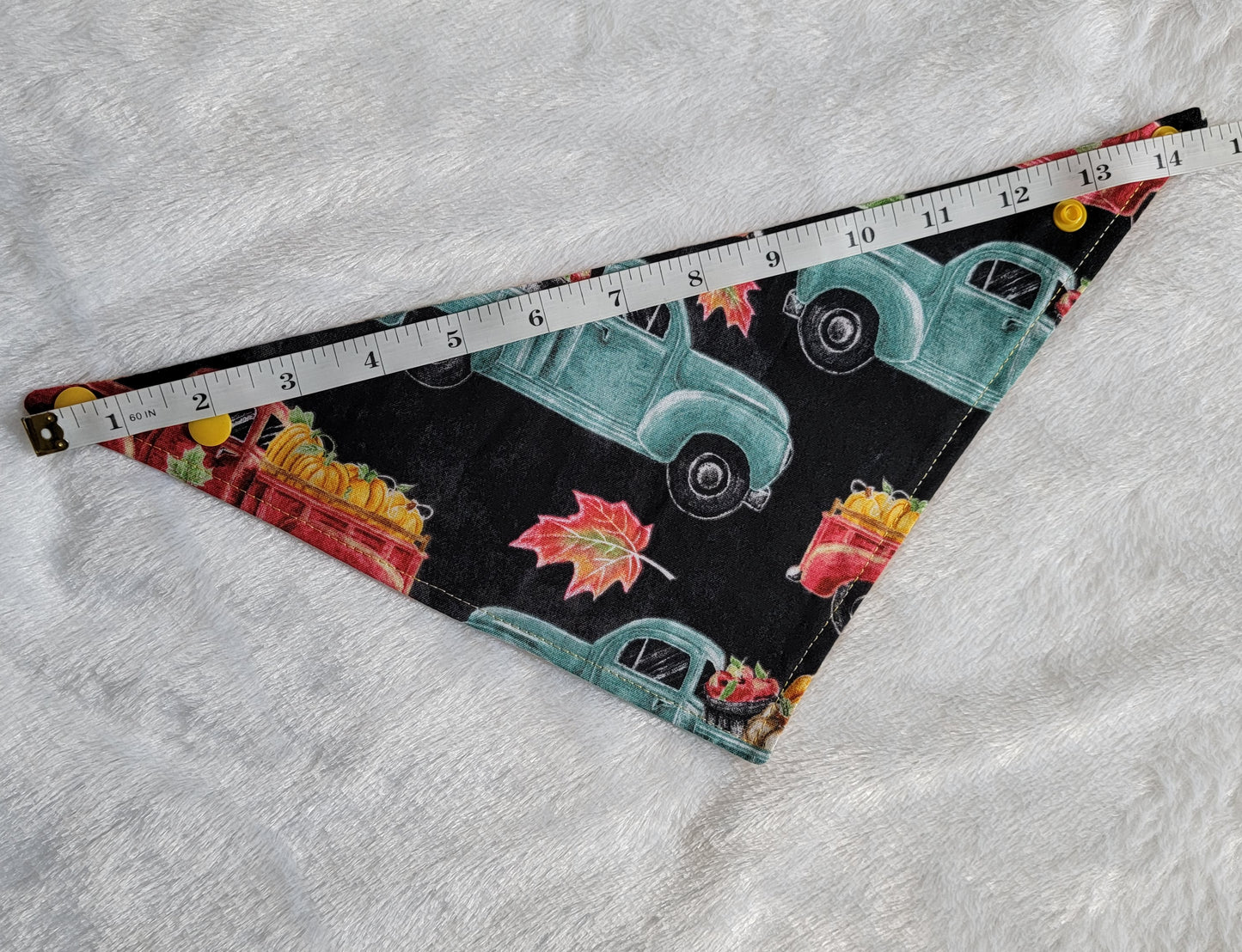 Bandana shown with measuring tape to show size is 14.5", print has trucks with pumpkins in them on black background.