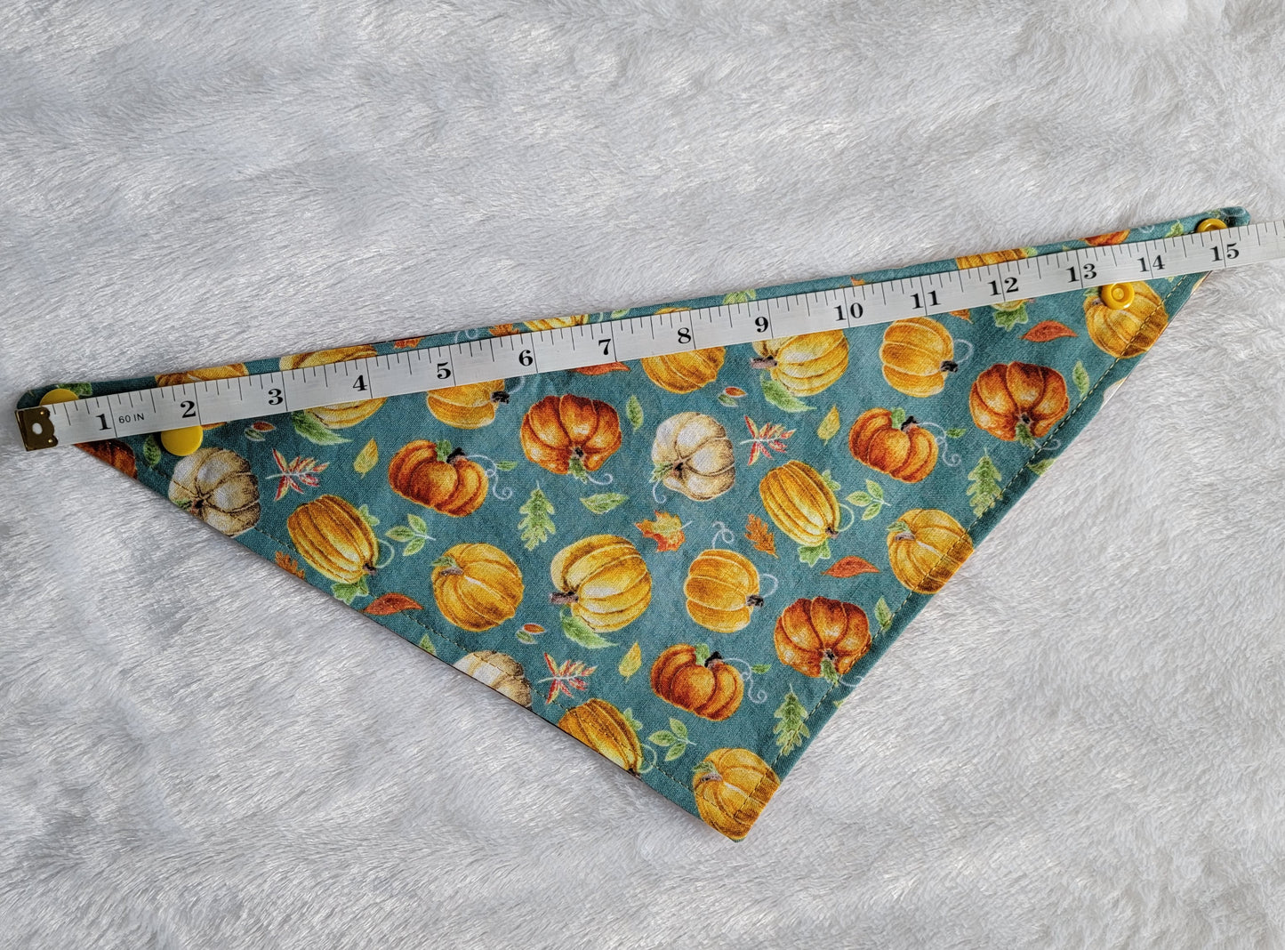 Bandana shown with measuring tape to show small size is 15.5", print is pumpkins on dusty blue background.