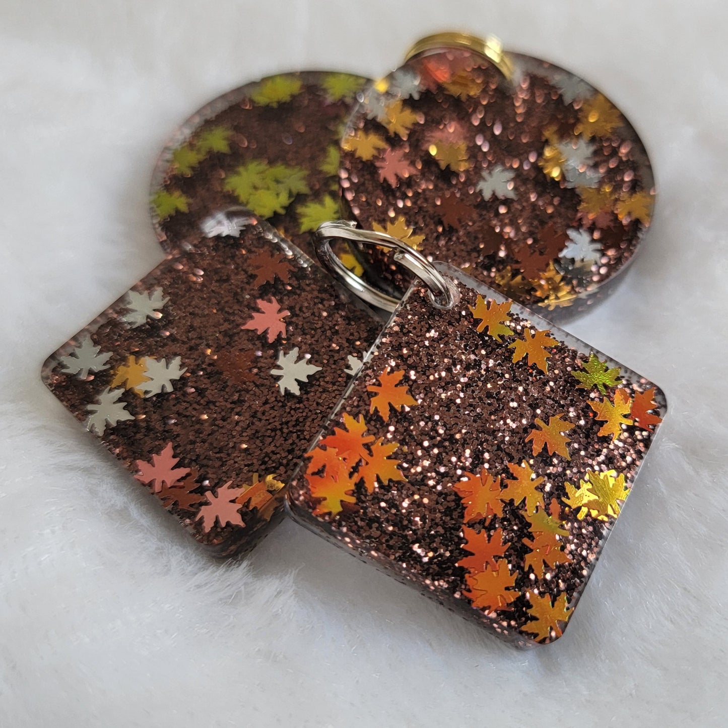 Four epoxy resin pieces, two square two round, with dark brown glitter and fall leaf shaped glitter.
