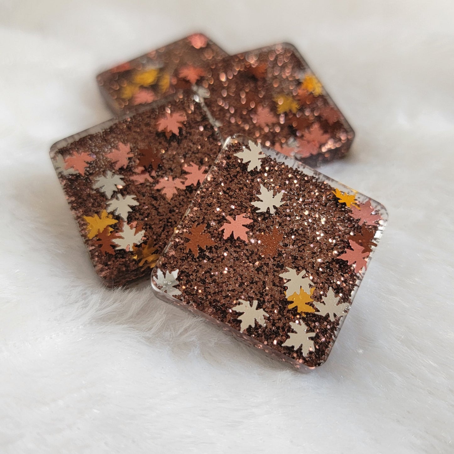 Four square epoxy resin pieces with dark brown glitter and fall leaf shaped glitter in shades of silver, copper and gold.