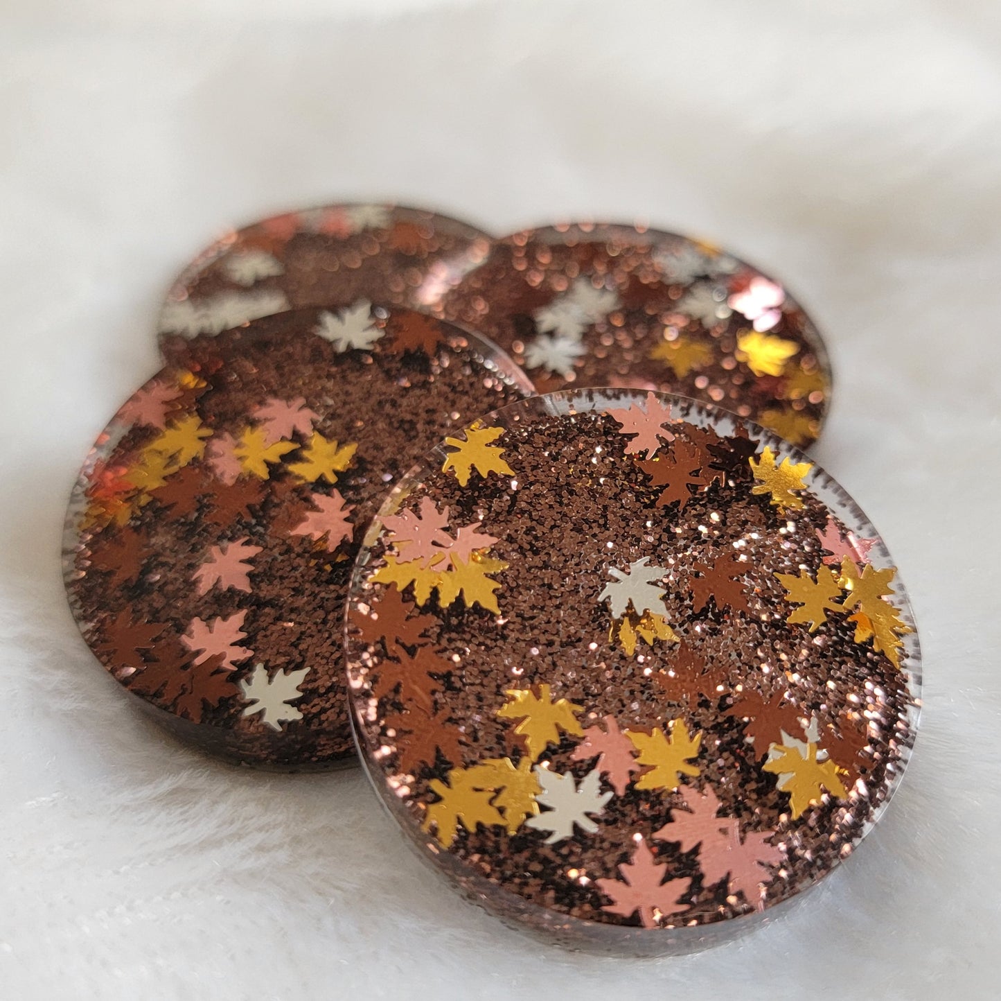 Four round epoxy resin pieces with dark brown glitter and fall leaf shaped glitter in shades of silver, copper and gold.