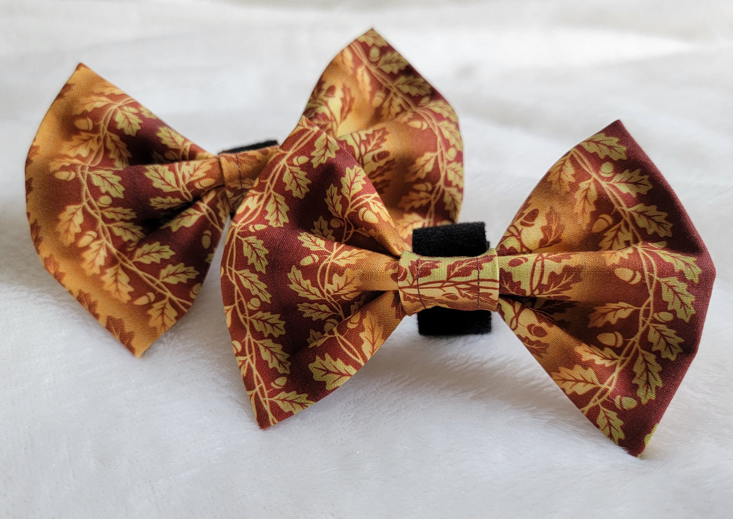 Two pet bows made of cotton with scrolling leaves and acorns print in light green, golden brown, and deep rusty brown.