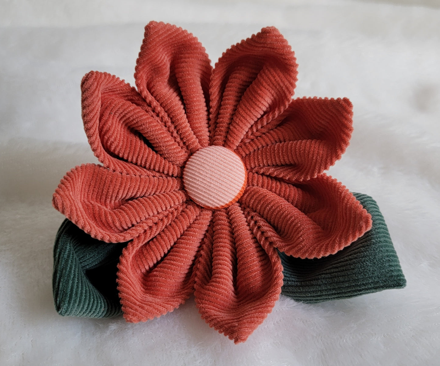 Fabric flower made with cotton corduroy, warm rusty red petals with a dusty pink center and two deep muted green leaves.