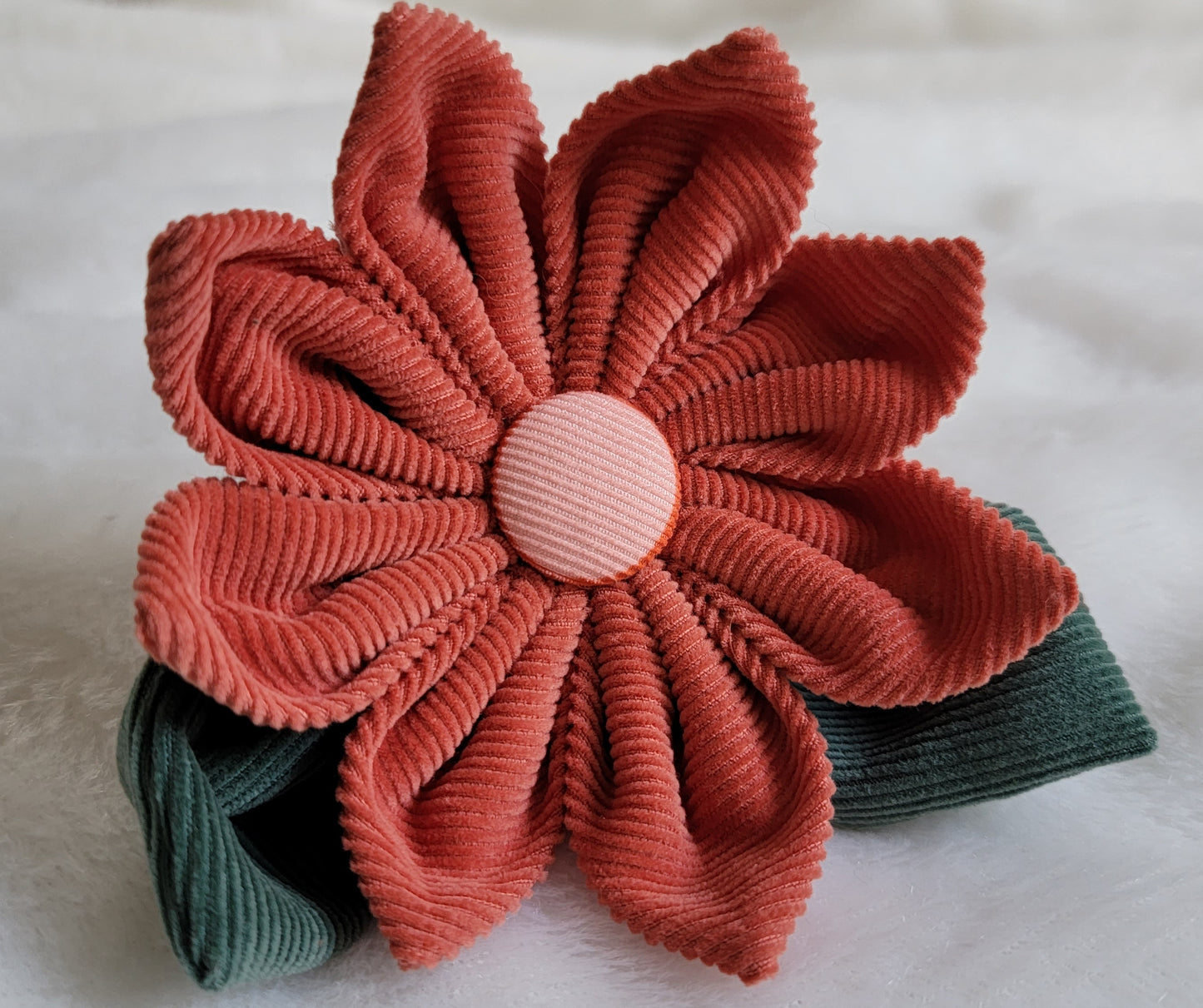 Fabric flower made with cotton corduroy, warm rusty red petals with a dusty pink center and two deep muted green leaves.