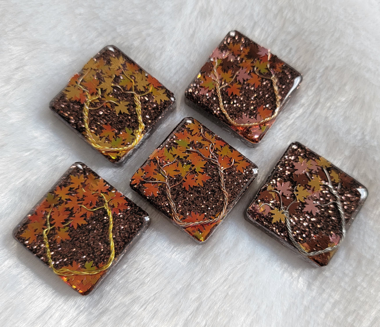Five square epoxy resin pieces with fall trees scene made of jewelry wire and leaf shaped glitter.