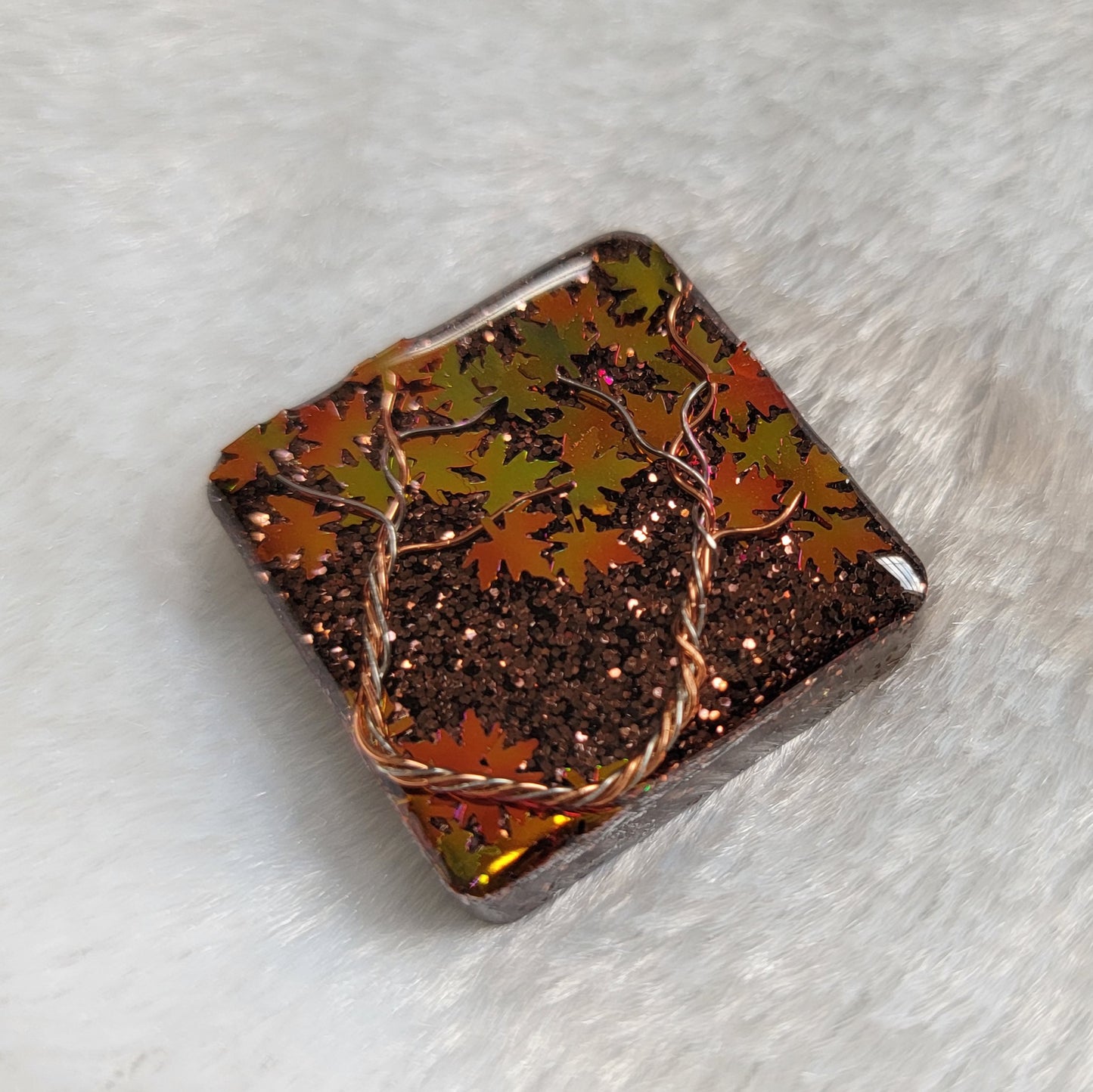 Square epoxy resin piece with fall trees scene made of copper and silver colored jewelry wire and holographic orange leaf shaped glitter.