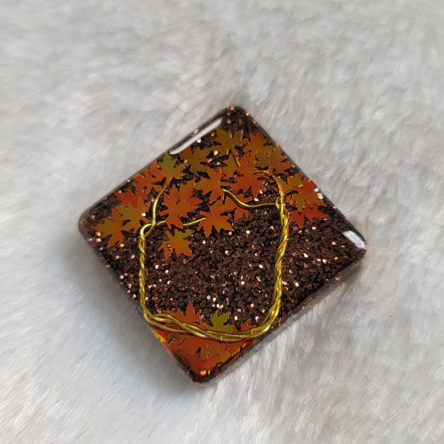 Square epoxy resin piece with fall trees scene made of gold colored jewelry wire and holographic orange leaf shaped glitter.