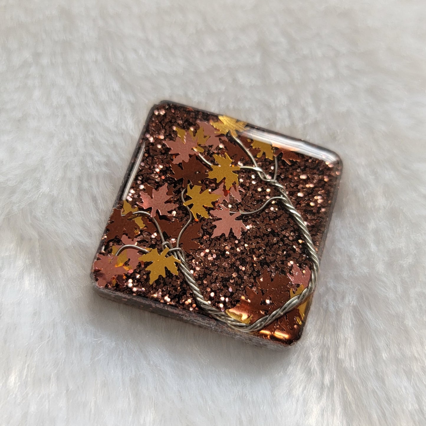 Square epoxy resin piece with fall trees scene made of silver colored jewelry wire and copper and gold leaf shaped glitter.