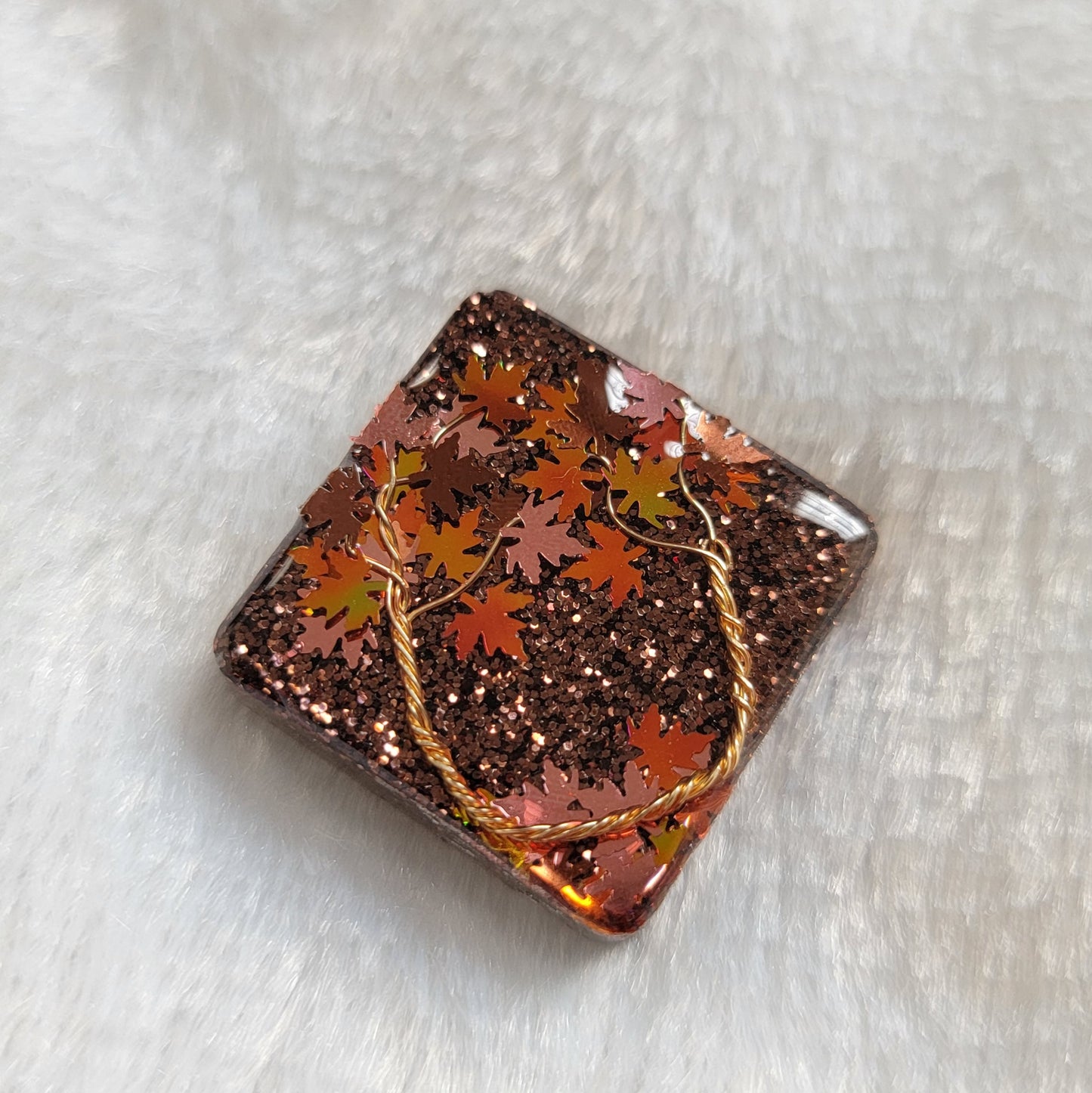 Square epoxy resin piece with fall trees scene made of copper colored jewelry wire and copper and holographic orange leaf shaped glitter.