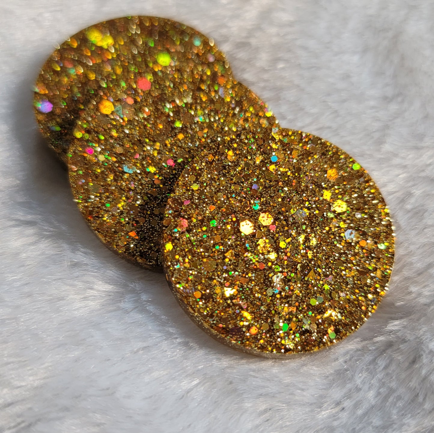 Three round epoxy resin pieces made with holographic gold glitter.