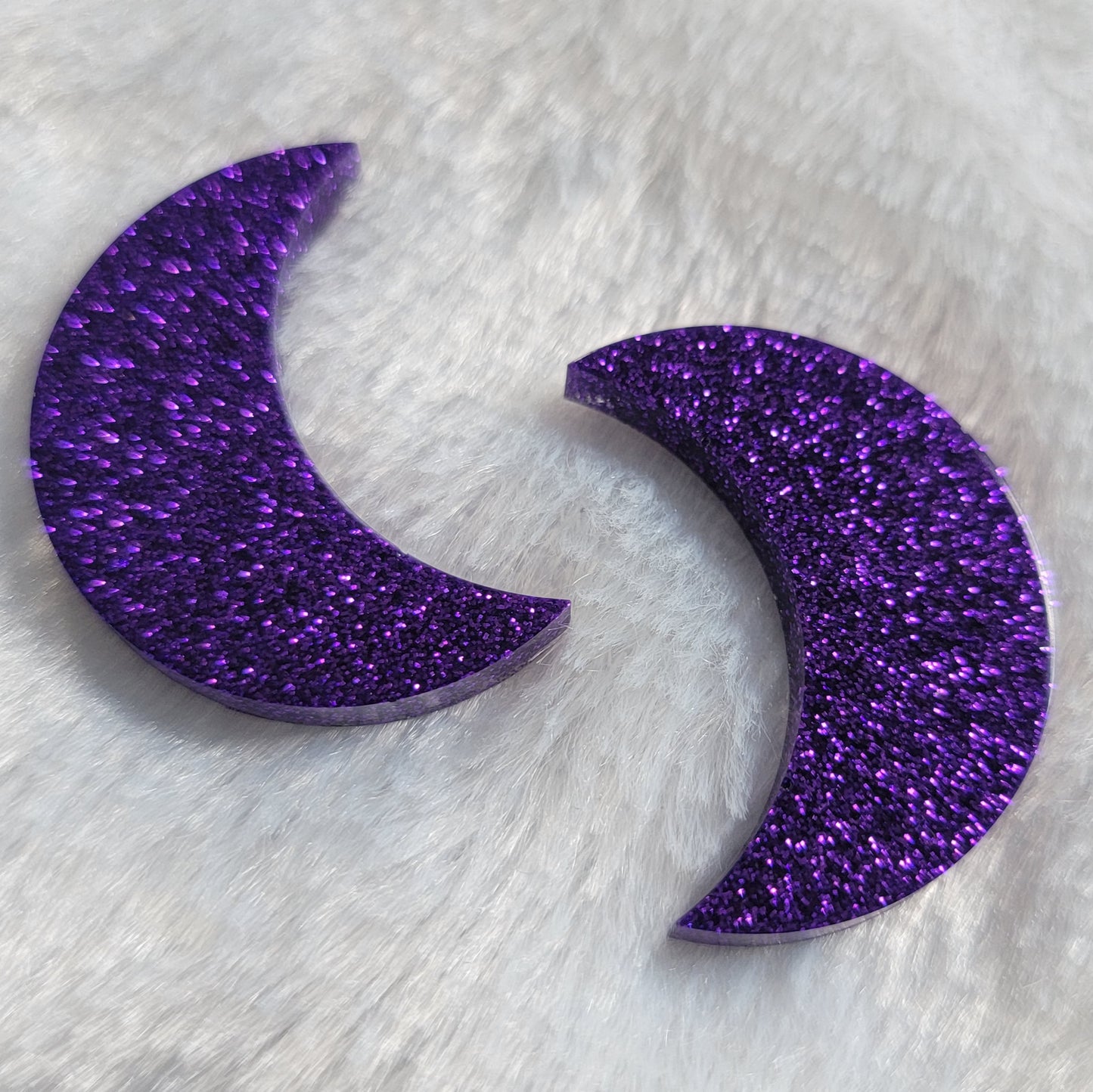 Two crescent moon shaped epoxy resin pieces made with deep purple glitter.