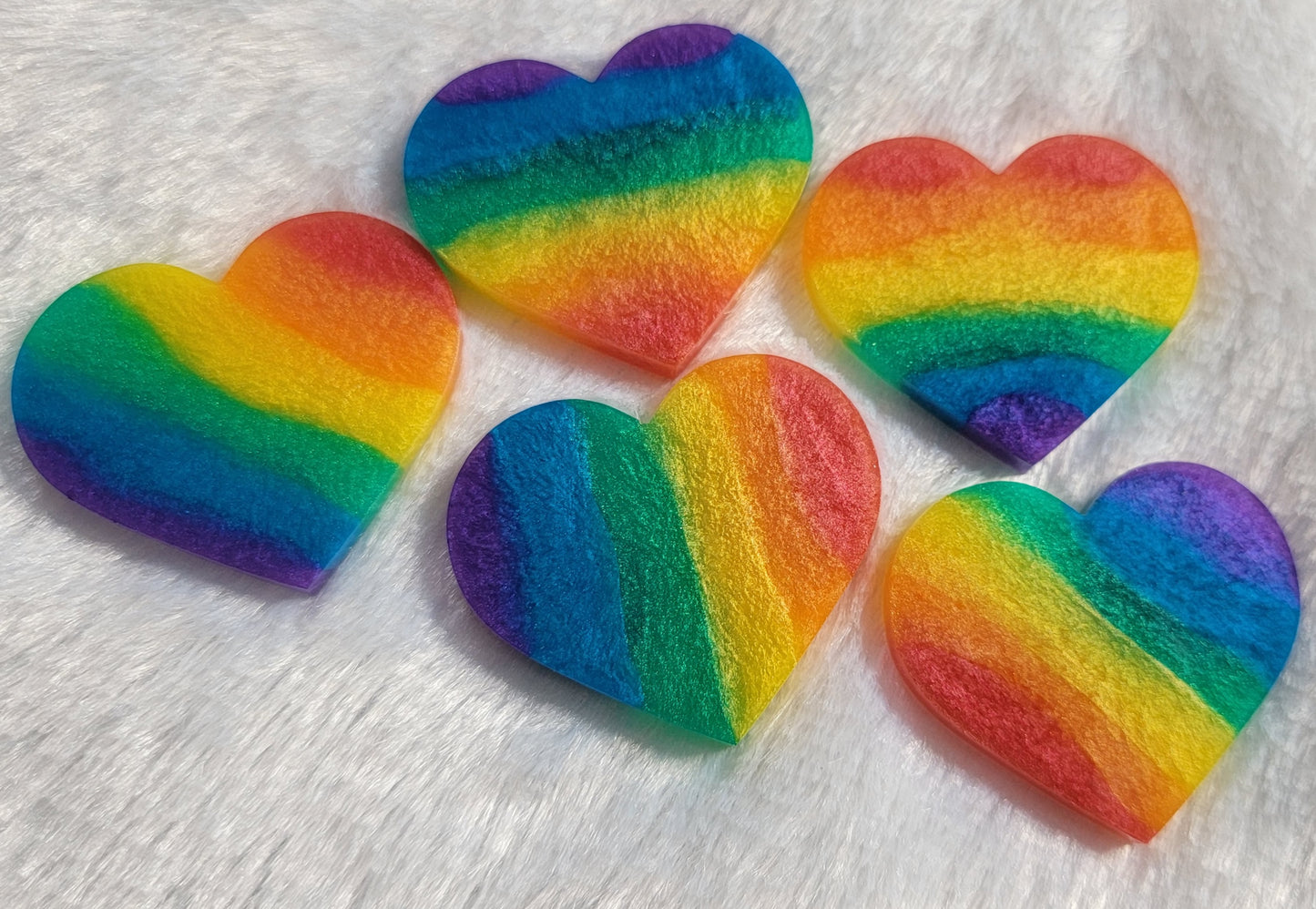 Five heart shaped epoxy resin pieces, each with rainbow stripes in shimmering mica pigments.