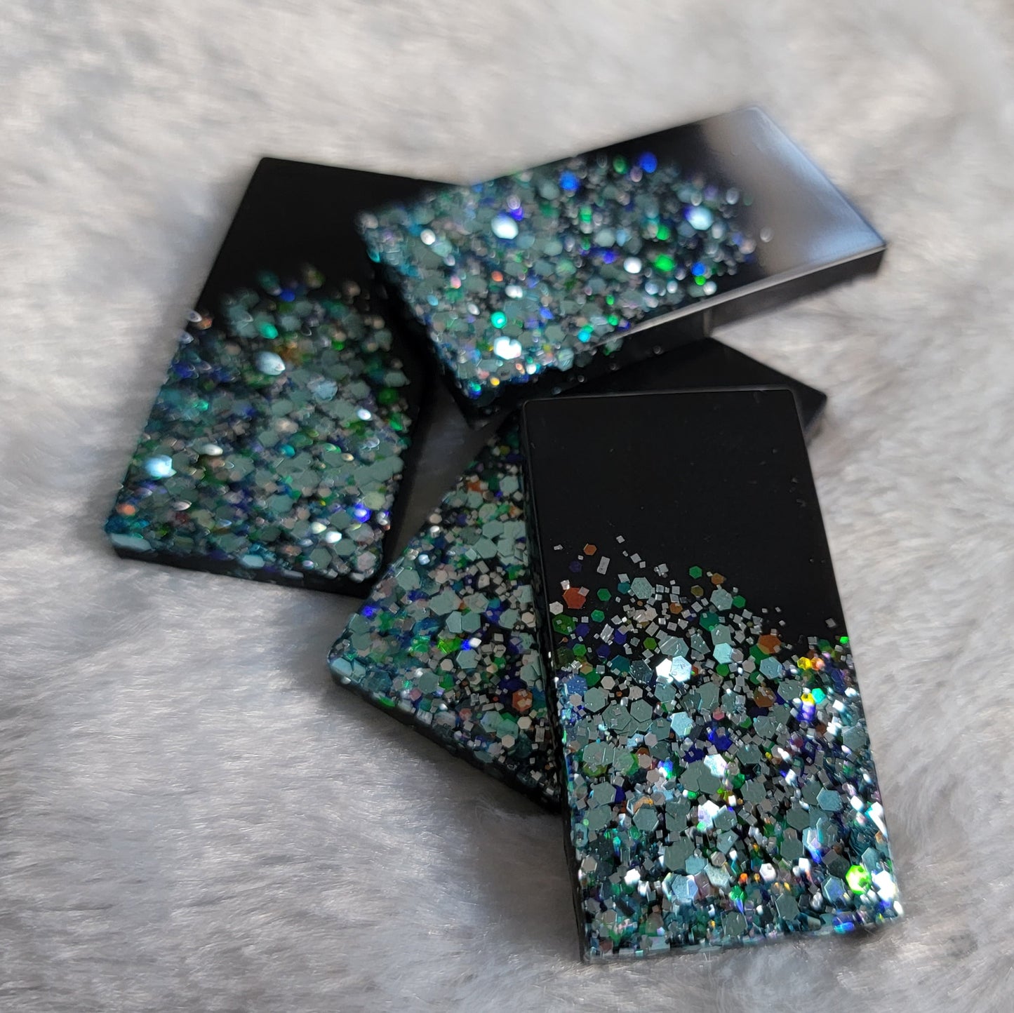 Four rectangular epoxy resin pieces, each is half black and half light blue holographic glitter.