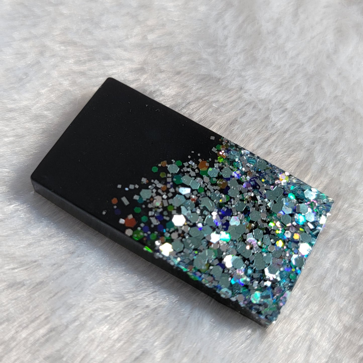 Rectangular epoxy resin piece that is half black and half light blue holographic glitter.