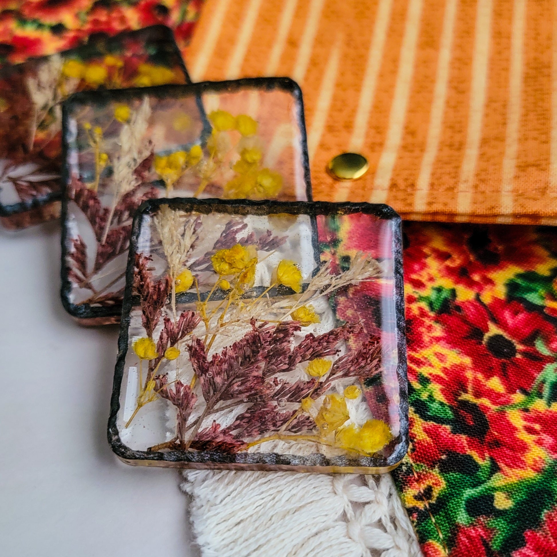 Square epoxy resin pieces with yellow, cream and red flowers cast in them, shown with coordinating rust orange floral bandanas.