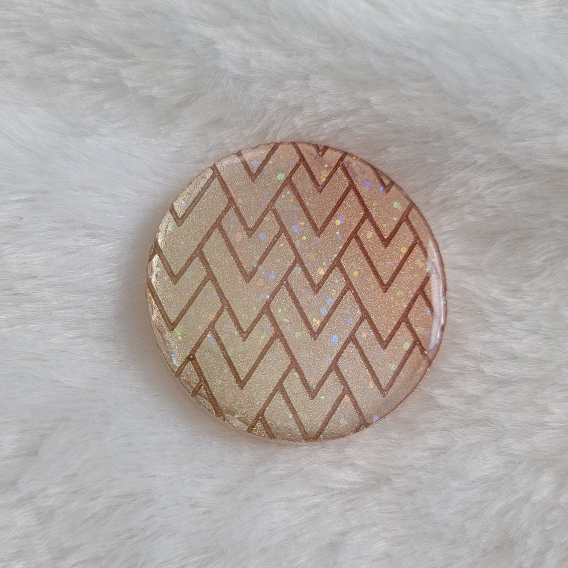 Round epoxy resin piece with glittering metallic ombre zig zag geometric pattern.