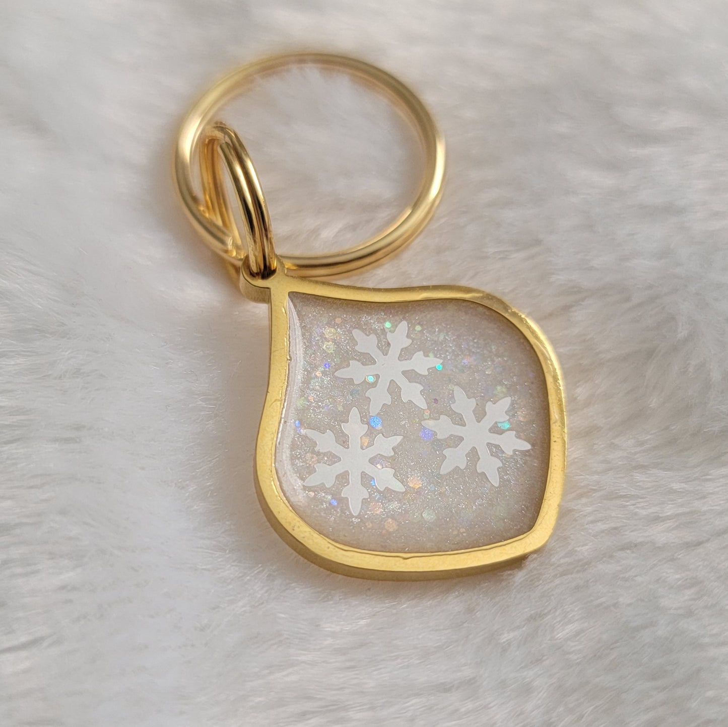 Small metal charm with white glittery snowflake epoxy resin filler.