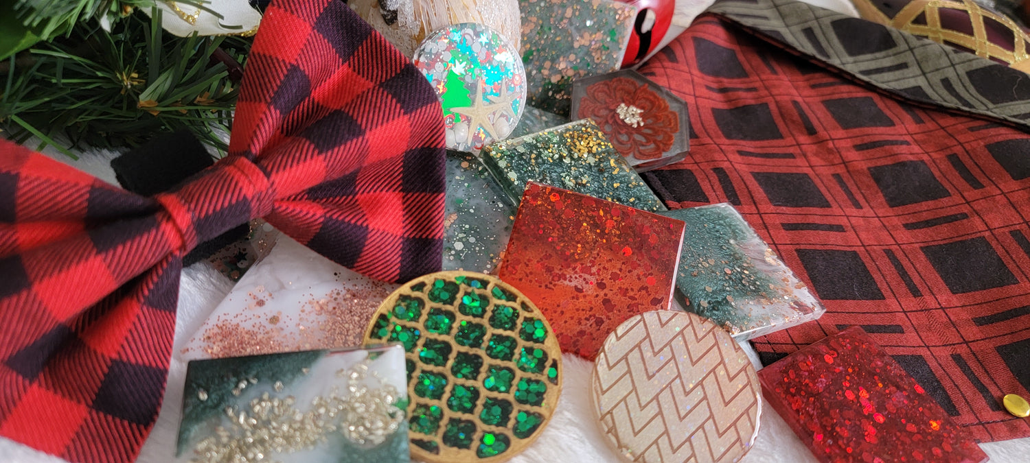 An array of handmade holiday items including epoxy resin tags and ornaments, a red plaid bowtie, and a red and green plaid bandana.