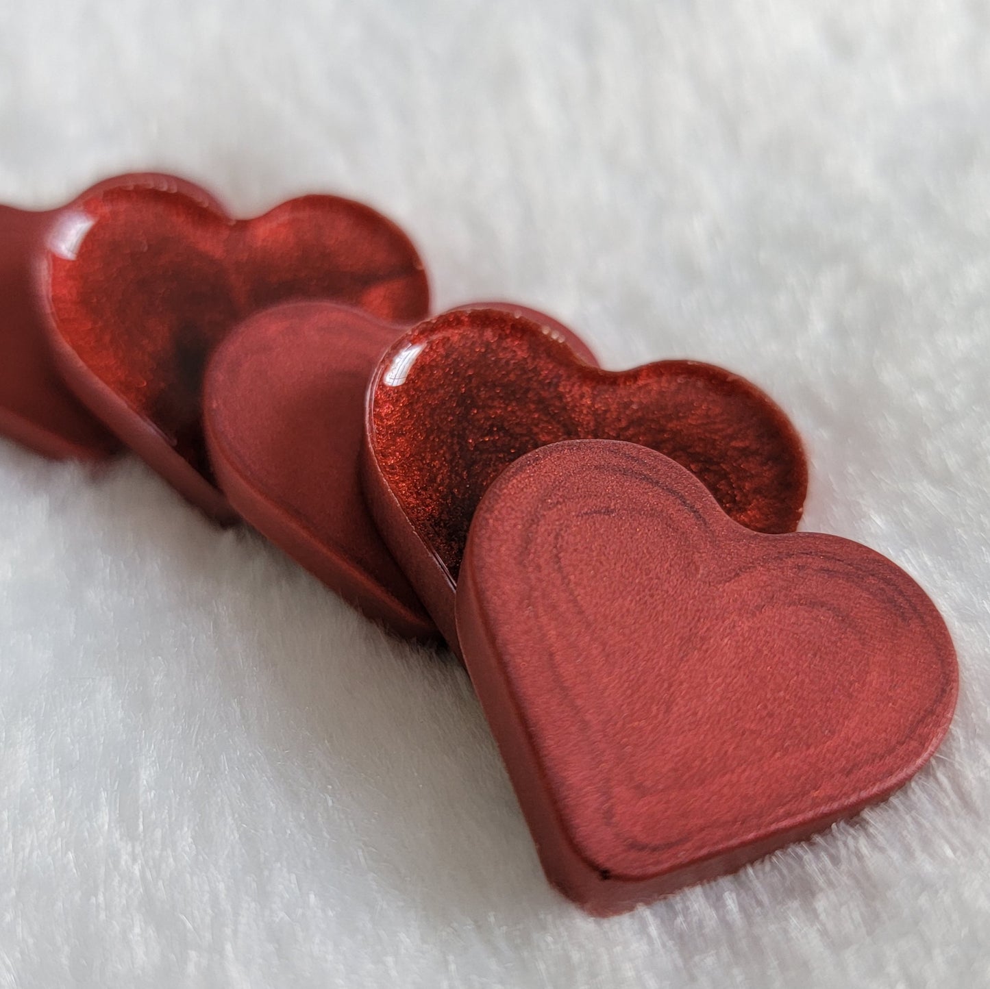 Mini heart shaped epoxy resin pieces with swirling candy red pigment.