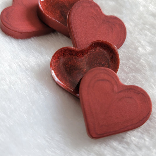 Mini heart shaped epoxy resin pieces with swirling candy red pigment.