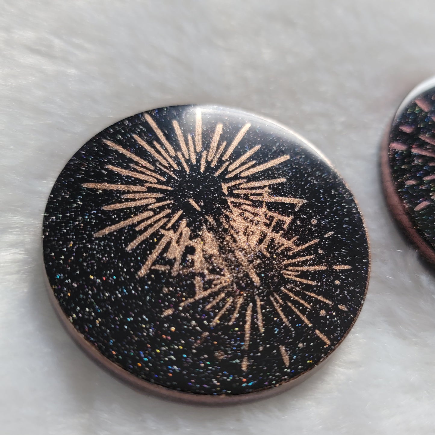 Round epoxy resin piece, translucent black with holographic sparkle and metallic fireworks design.