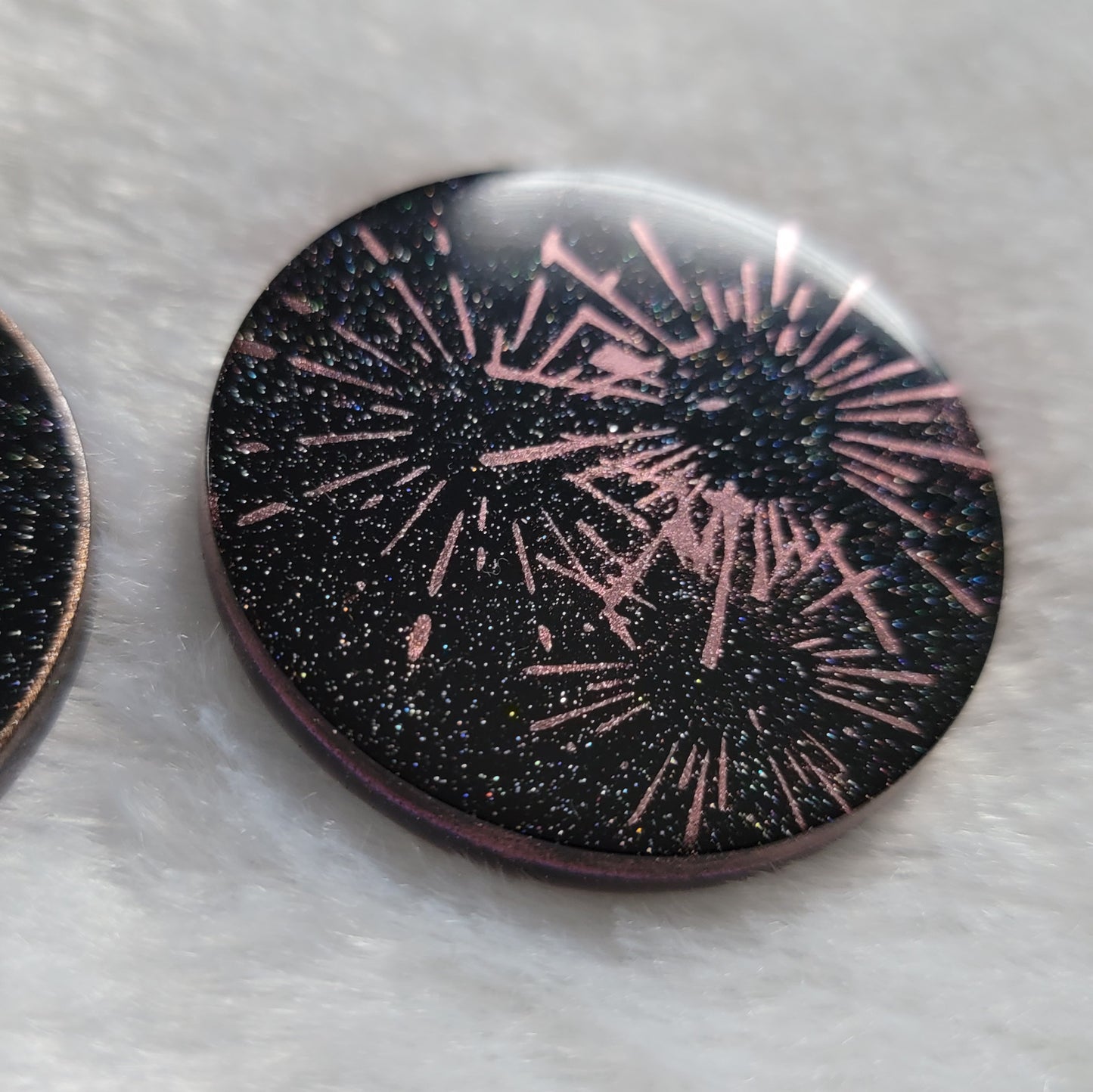 Round epoxy resin piece, translucent black with holographic sparkle and metallic fireworks design.