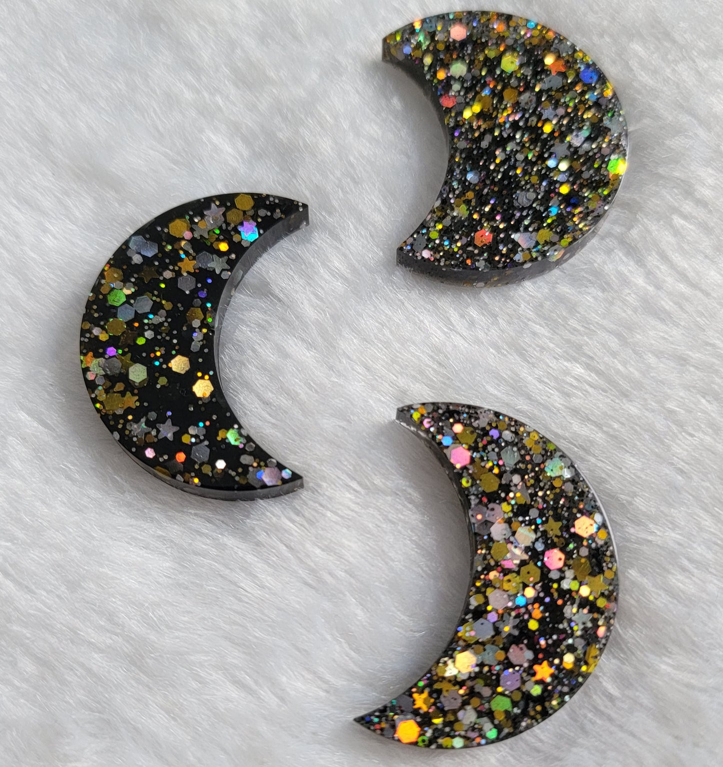 Three crescent moon shaped epoxy resin pieces, black with silver and gold holographic glitter.