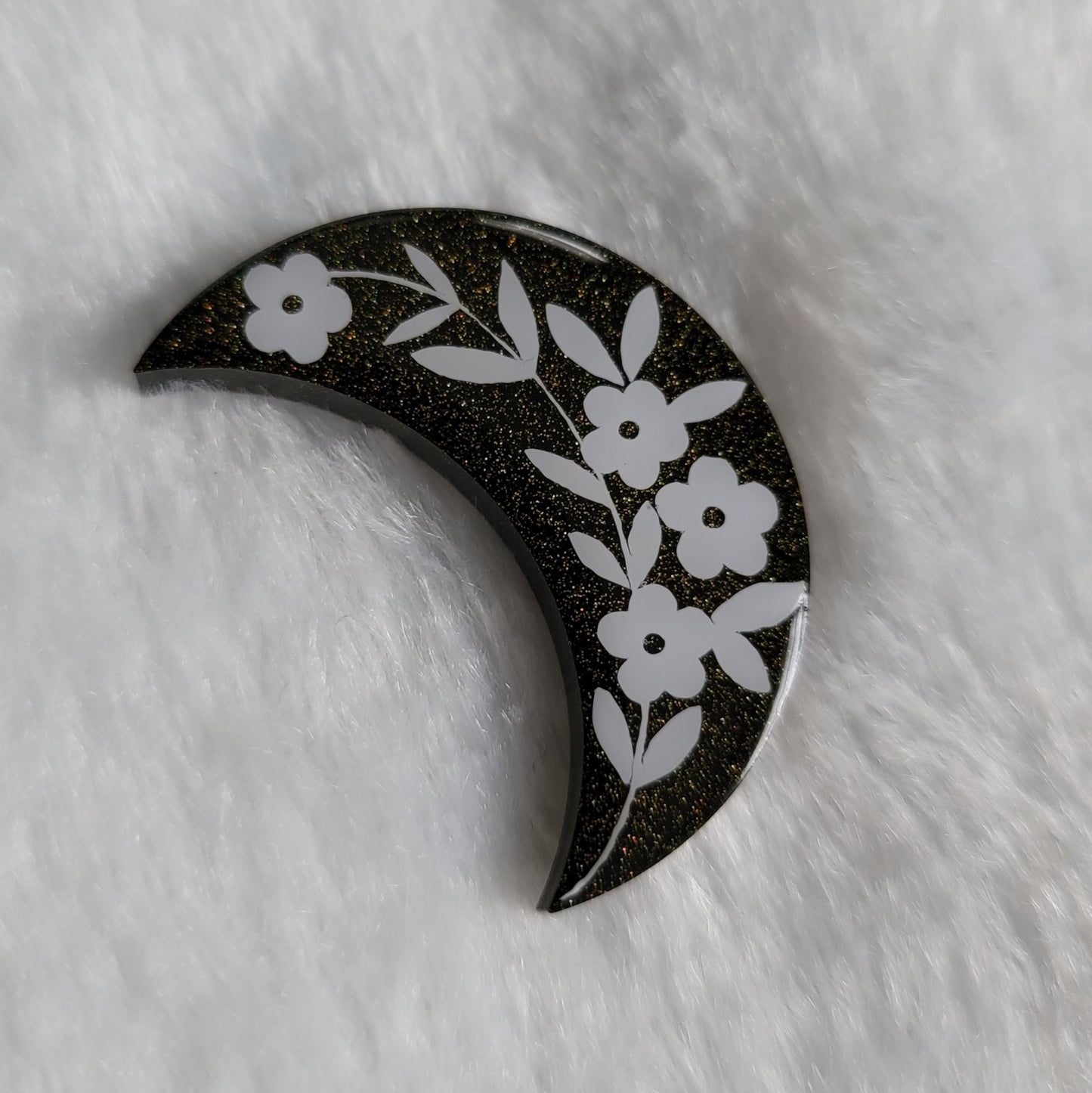 Crescent moon shaped epoxy resin piece, black with gold holographic sparkle and floral design in white vinyl.