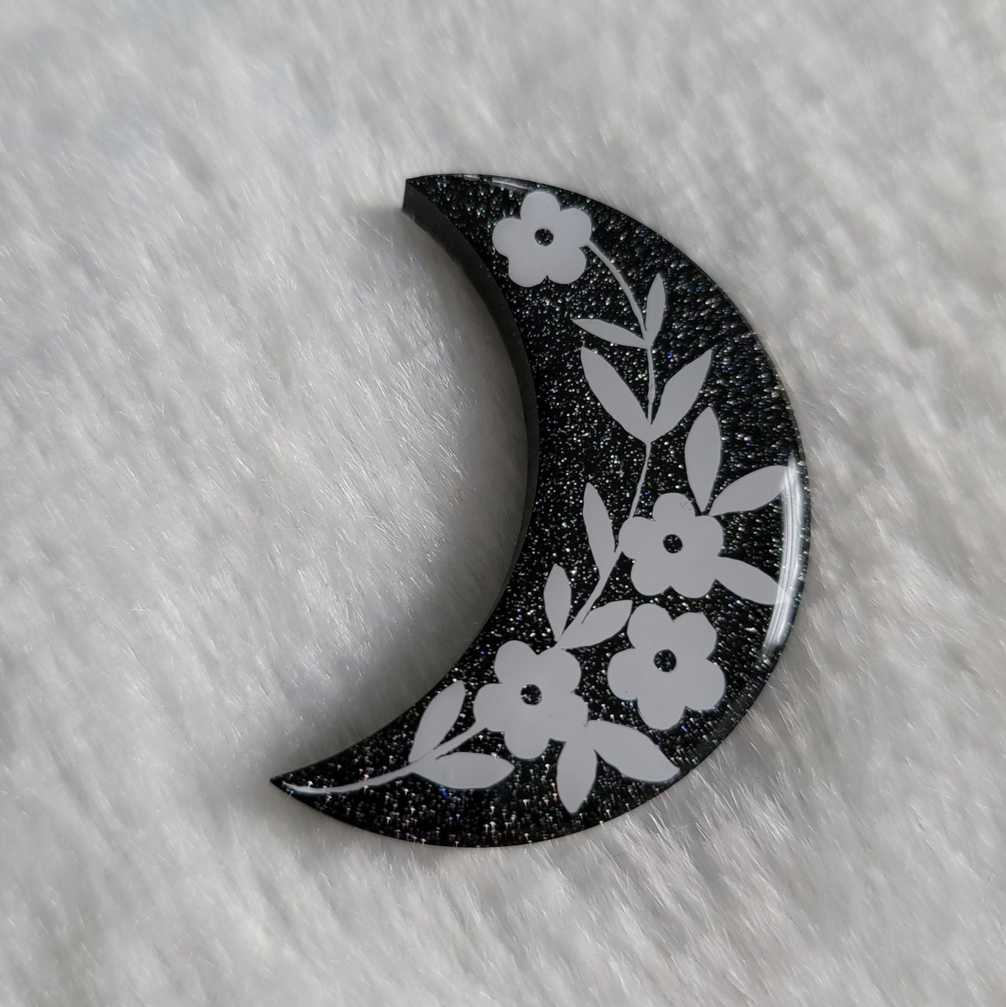 Crescent moon shaped epoxy resin piece, black with silver holographic sparkle and floral design in white vinyl.