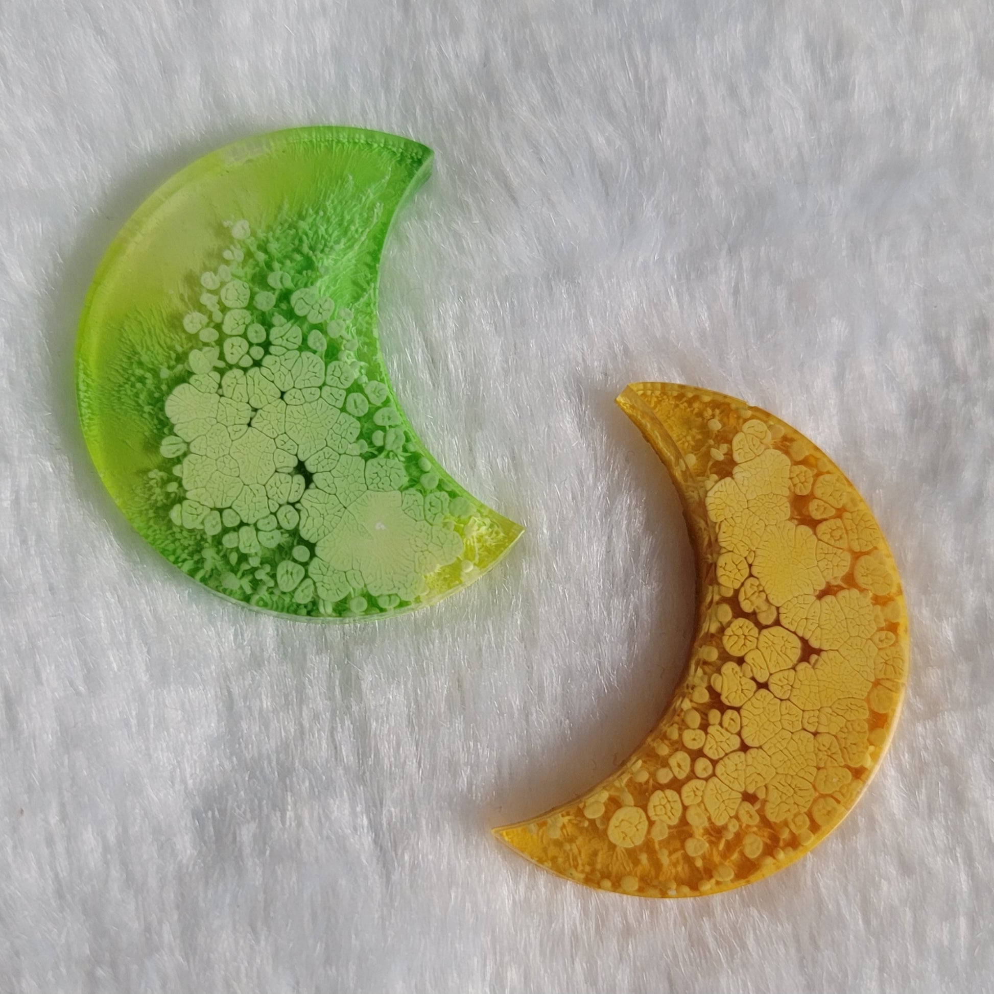 Crescent moon shaped epoxy resin pieces, thicker crescent in lime green ink and standard crescent in mango orange ink.