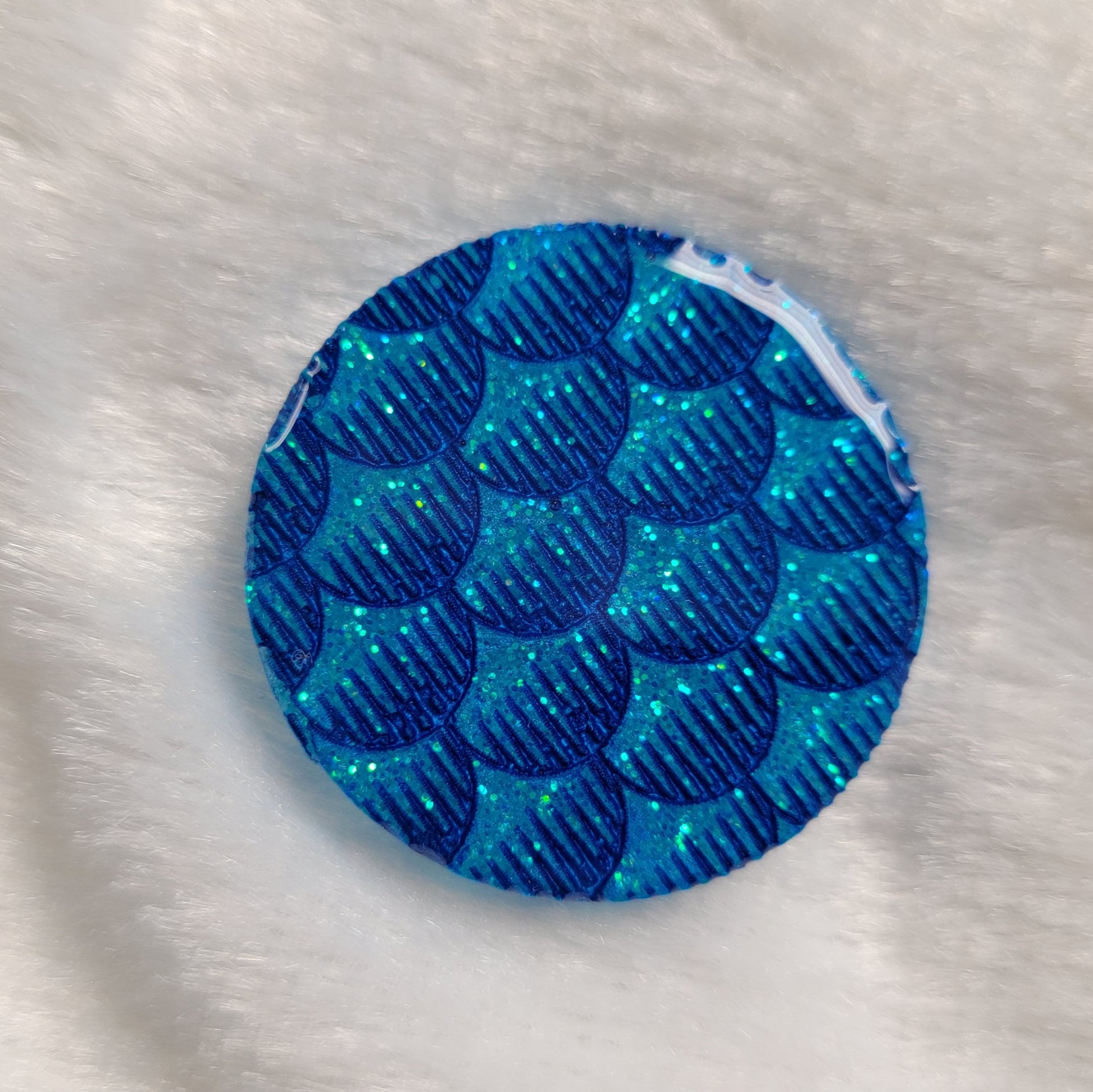 Round epoxy resin piece, light aqua blue glitter with dark blue details of fish scales design.