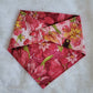 Reversible dog bandana with pink lilies print, pink plastic snap closure, and red faux leather logo tag.