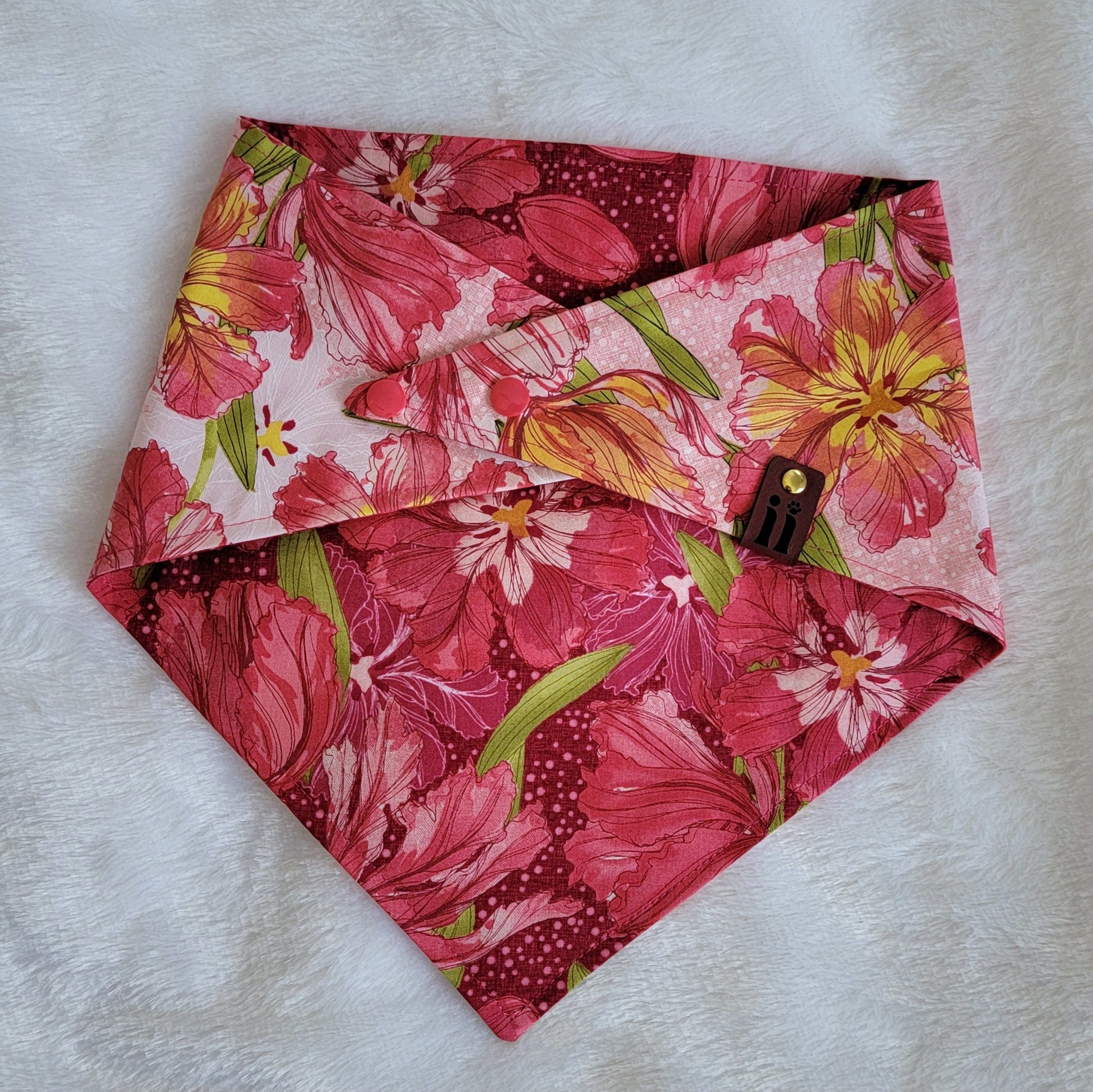 Reversible dog bandana with pink lilies print, pink plastic snap closure, and red faux leather logo tag.