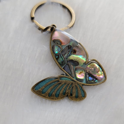 Antique bronze tone metal butterfly charm with rainbow shells and epoxy resin filler.