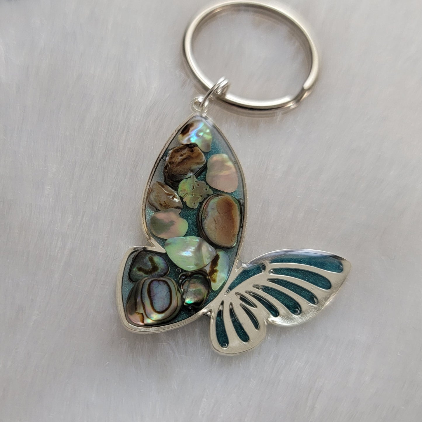 Silver tone metal butterfly charm with rainbow shells and epoxy resin filler.