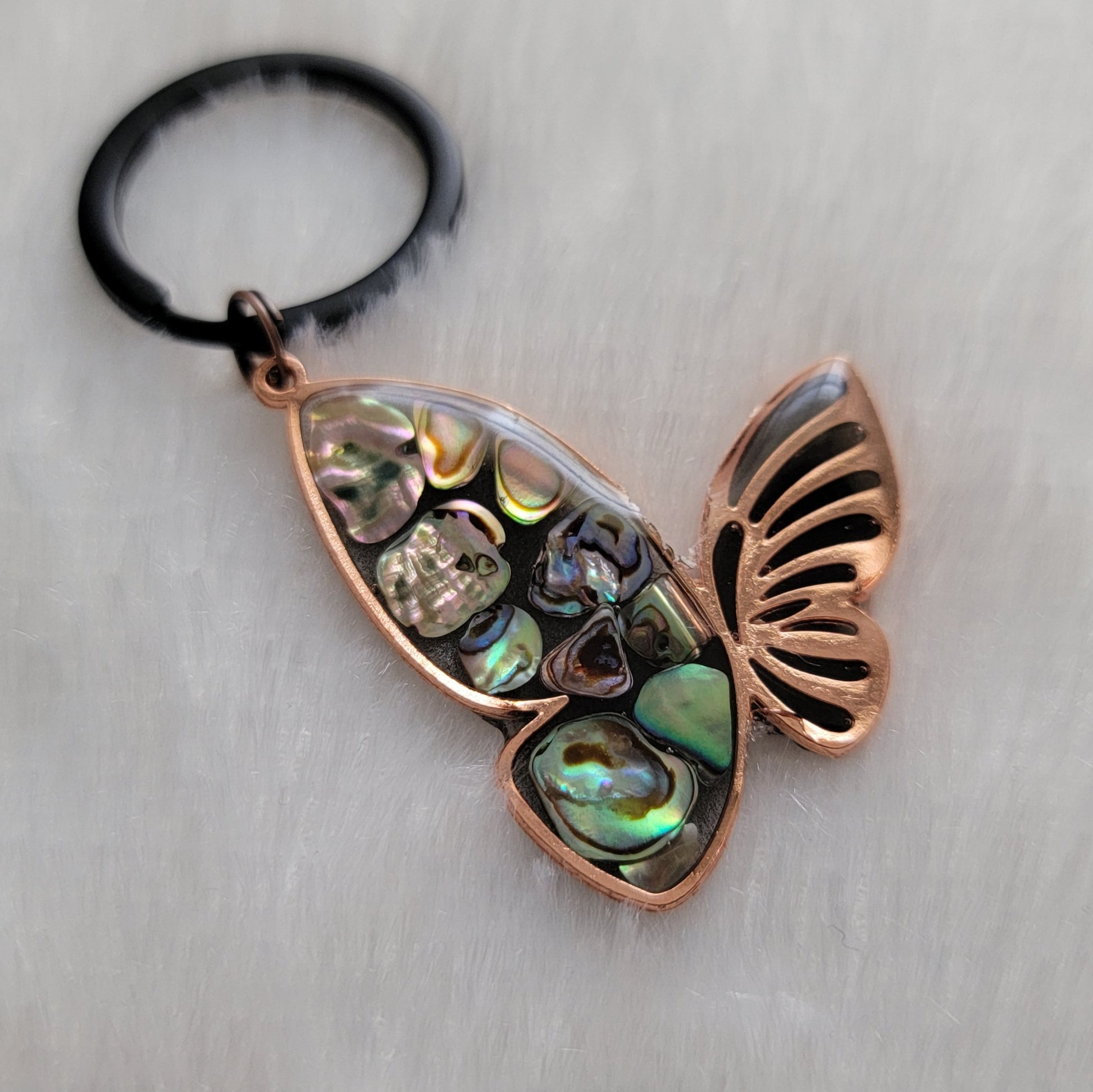 Copper tone metal butterfly charm with rainbow shells and epoxy resin filler.