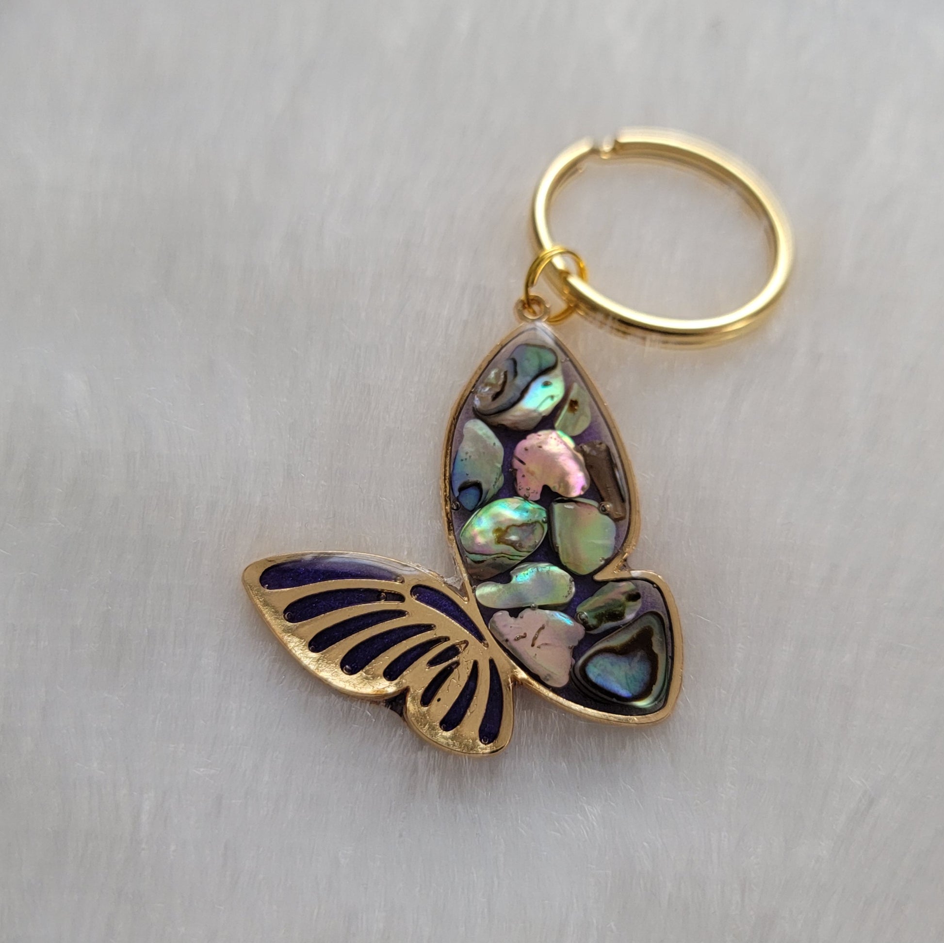 Gold tone metal butterfly charm with rainbow shells and epoxy resin filler.