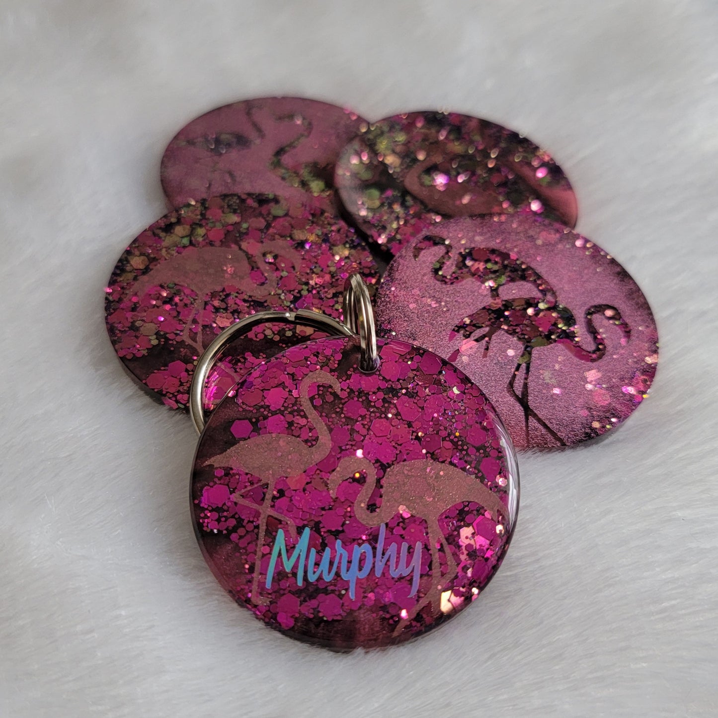 Round epoxy resin pieces, hot pink glitter with metallic flamingo designs. One shown with personalization in silver holographic vinyl.